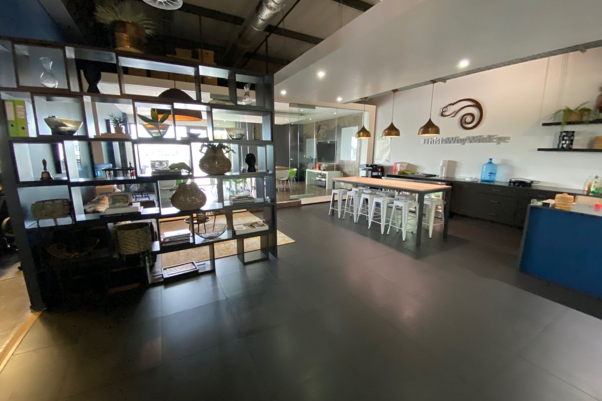 Modern open-plan office space featuring industrial-style exposed ceiling ducting, sleek tiled flooring, integrated cabinetry, and contemporary pendant lighting.