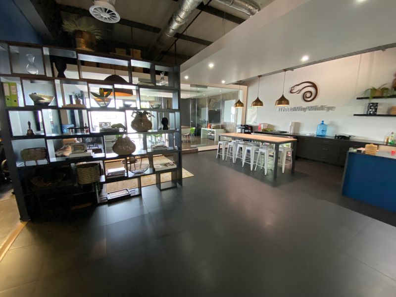 Modern open-plan office space featuring industrial-style exposed ceiling ducting, sleek tiled flooring, integrated cabinetry, and contemporary pendant lighting.