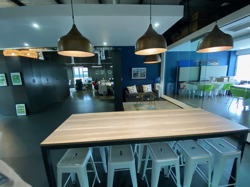 Modern open-plan office space featuring industrial-style pendant lighting, glass-partitioned meeting areas, built-in storage lockers, and exposed ceiling infrastructure.