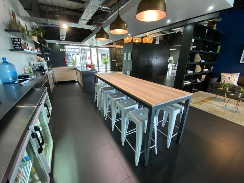Modern open-plan office breakout area featuring industrial-style exposed ceilings, sleek built-in cabinetry, integrated refrigeration, and a central communal high-top table.