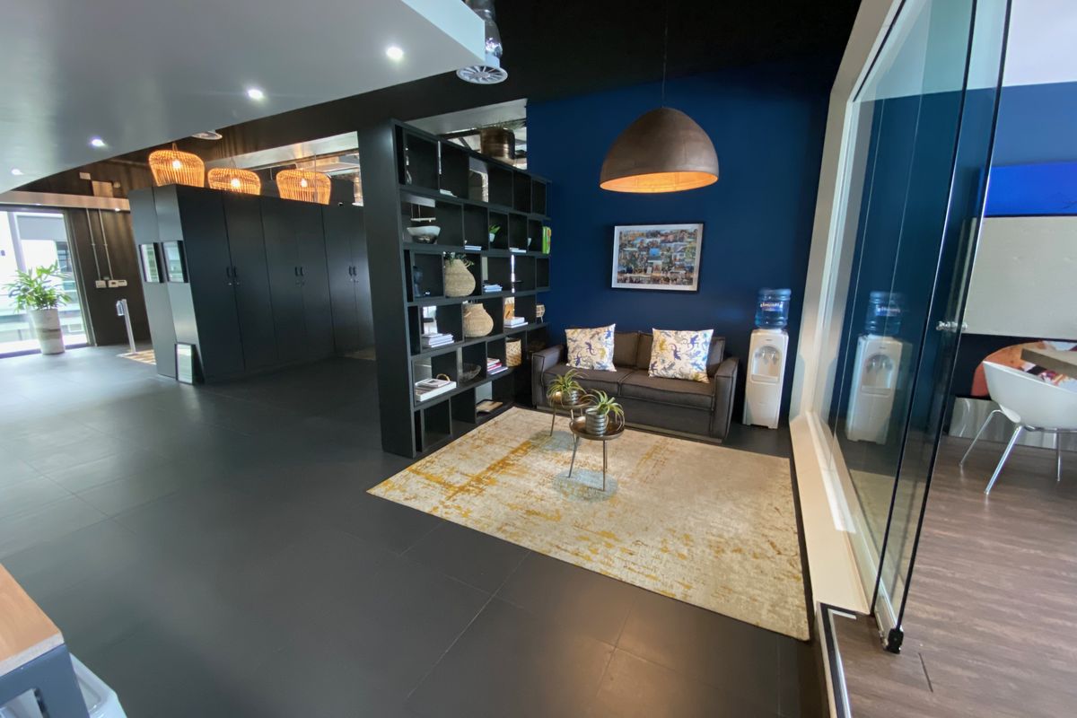 A modern office reception or breakout area featuring dark tiled flooring, a built-in shelving unit, and a glass partition wall with contemporary lighting.