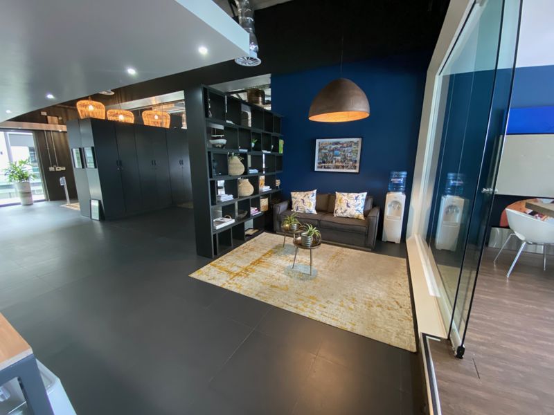 A modern office reception or breakout area featuring dark tiled flooring, a built-in shelving unit, and a glass partition wall with contemporary lighting.