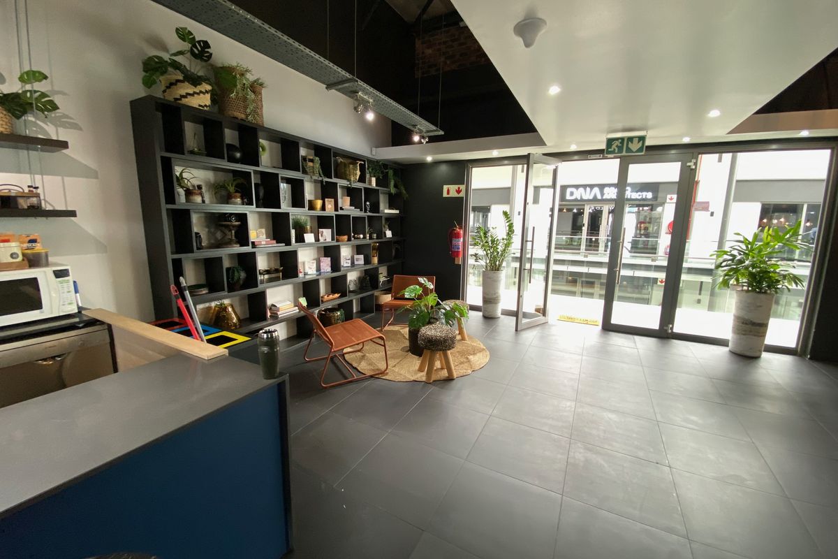 Modern office space featuring dark tiled flooring, built-in shelving, exposed industrial ceiling ducting, and large glass doors providing natural light and exterior access.
