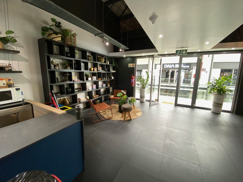 Modern office space featuring dark tiled flooring, built-in shelving, exposed industrial ceiling ducting, and large glass doors providing natural light and exterior access.