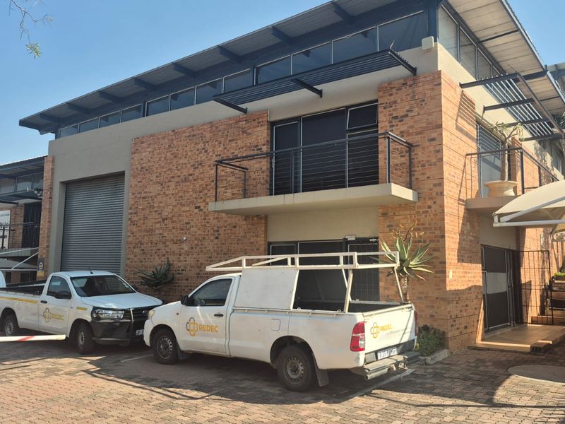 Front elevation of a modern industrial property featuring face brick construction, a roller shutter door, and an upper-level balcony with metal railings.