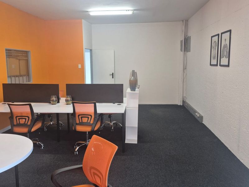 A functional office space featuring carpeted flooring, bright orange accent walls, and integrated lighting, suitable for a professional work environment.
