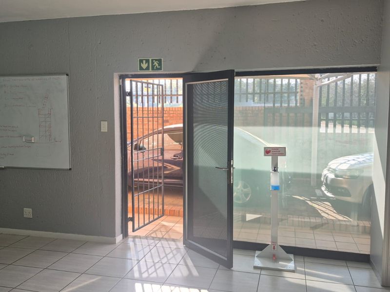 An industrial entry area featuring tiled flooring, a security gate, and a large glass door providing access to the exterior parking area.
