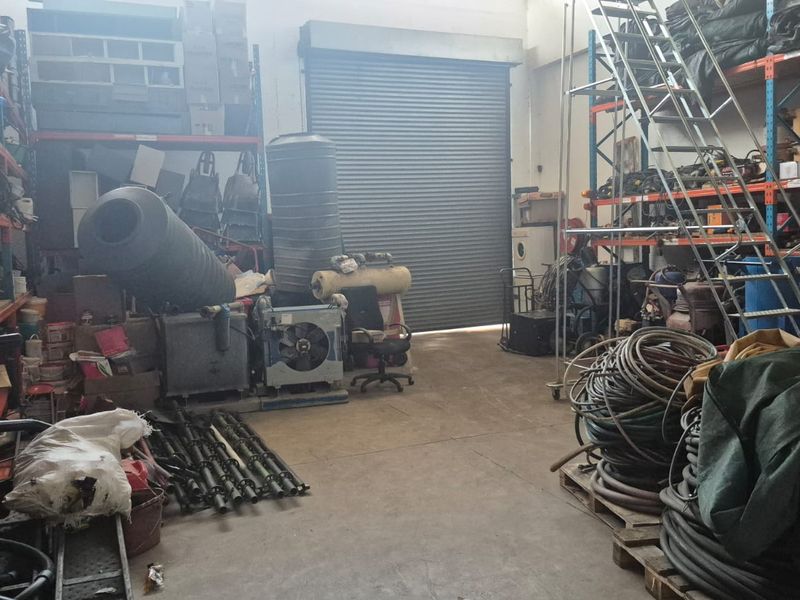 Industrial utility space featuring a large roller shutter door, concrete flooring, and extensive built-in industrial shelving units for storage.