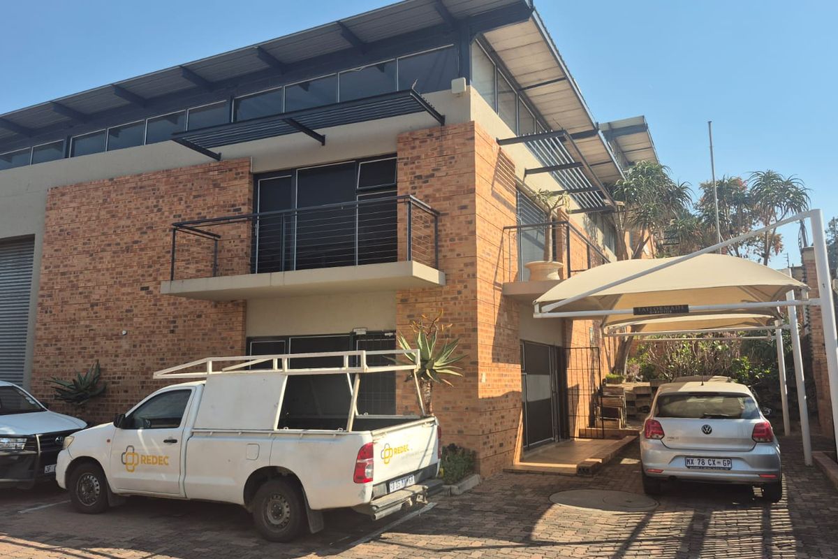 Front elevation of a multi-level industrial building featuring face brick construction, a roller shutter door, balcony access, and a covered parking area.