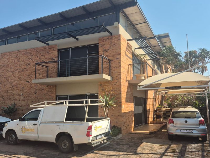 Front elevation of a multi-level industrial building featuring face brick construction, a roller shutter door, balcony access, and a covered parking area.