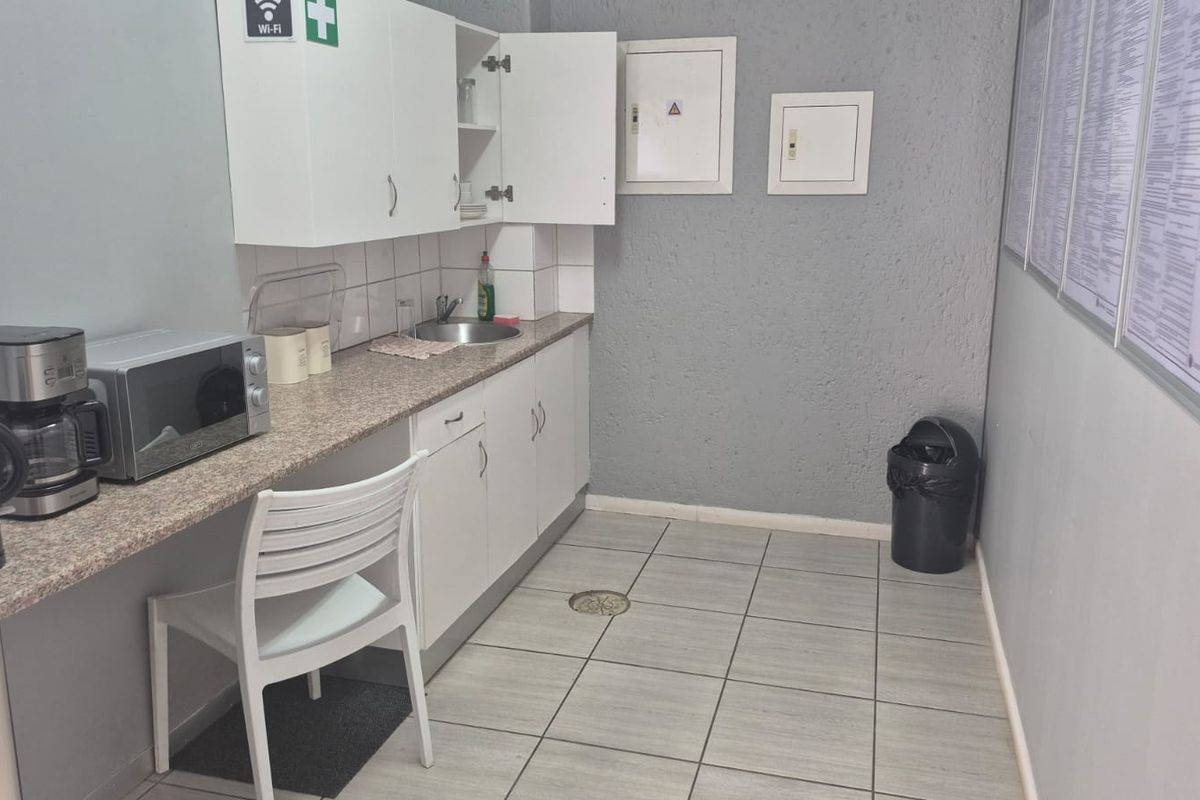 A functional kitchenette area featuring built-in cabinetry, a laminate countertop with an integrated sink, and durable tiled flooring in an industrial setting.