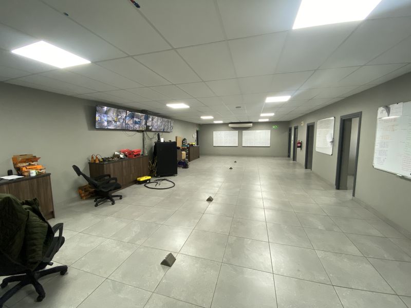 A spacious, well-lit industrial utility or control room featuring tiled flooring, a suspended ceiling, and a wall-mounted security monitoring system.
