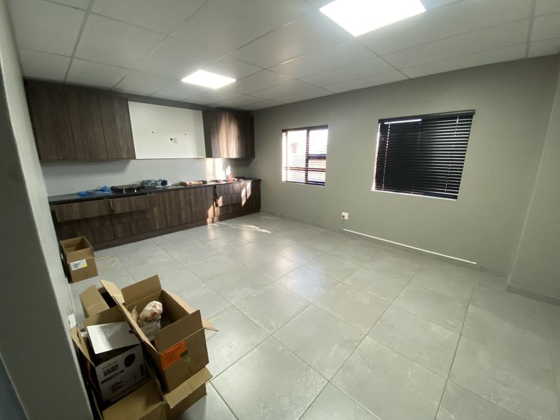 A clean, modern industrial kitchen space featuring dark wood-finish cabinetry, grey tiled flooring, and recessed ceiling lighting, offering a functional and neutral workspace.