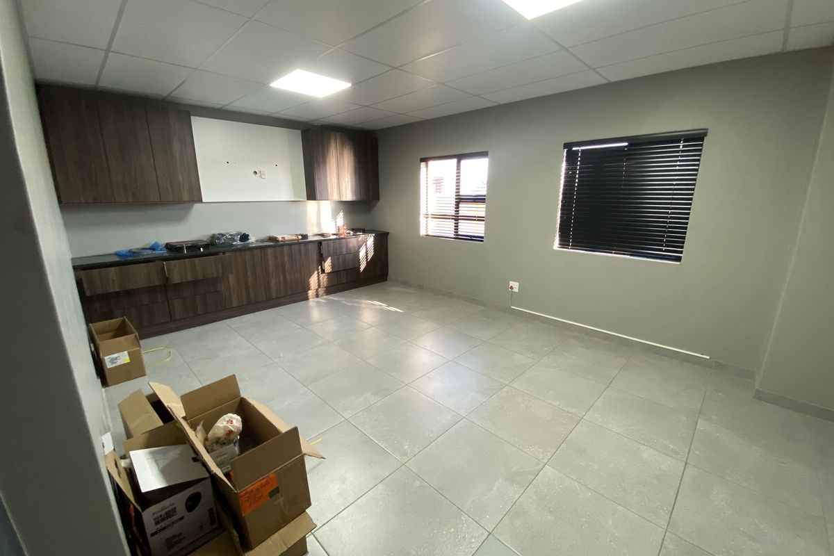 A clean, modern industrial kitchen space featuring dark wood-finish cabinetry, grey tiled flooring, and recessed ceiling lighting, offering a functional and neutral workspace.