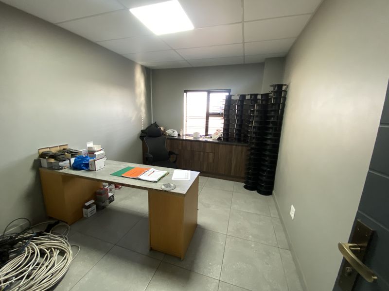 A functional office space featuring tiled flooring, a suspended ceiling with recessed lighting, and built-in cabinetry under a window with security bars.