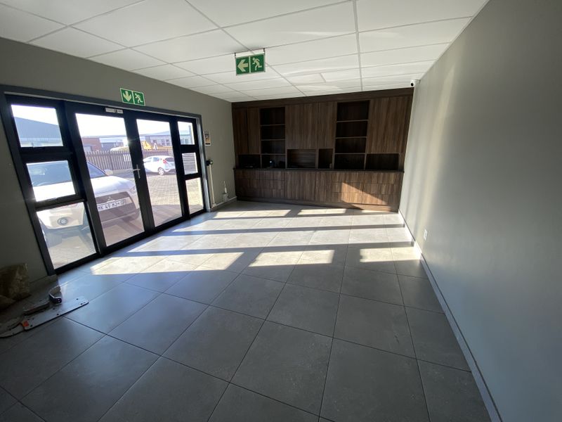 A bright, modern office space featuring tiled flooring, a suspended ceiling, and extensive built-in wooden cabinetry, with direct access through glass doors.