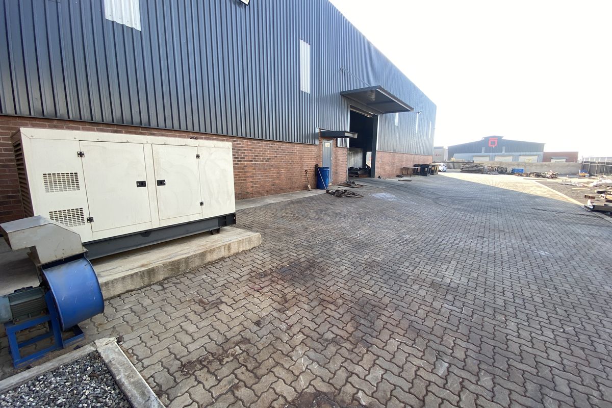 Rear industrial yard featuring paved surfacing, brick and metal cladding facade, and a fixed industrial generator unit.