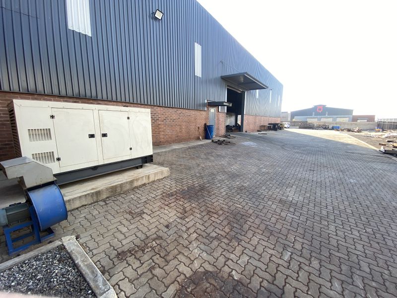 Rear industrial yard featuring paved surfacing, brick and metal cladding facade, and a fixed industrial generator unit.