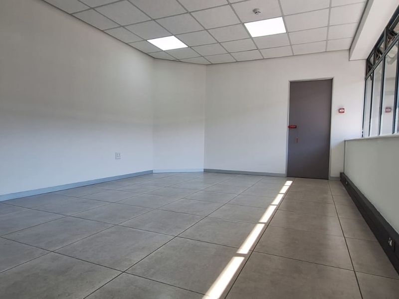 A bright, vacant office space featuring modern tiled flooring, a suspended ceiling with recessed lighting, and an internal glass partition wall.