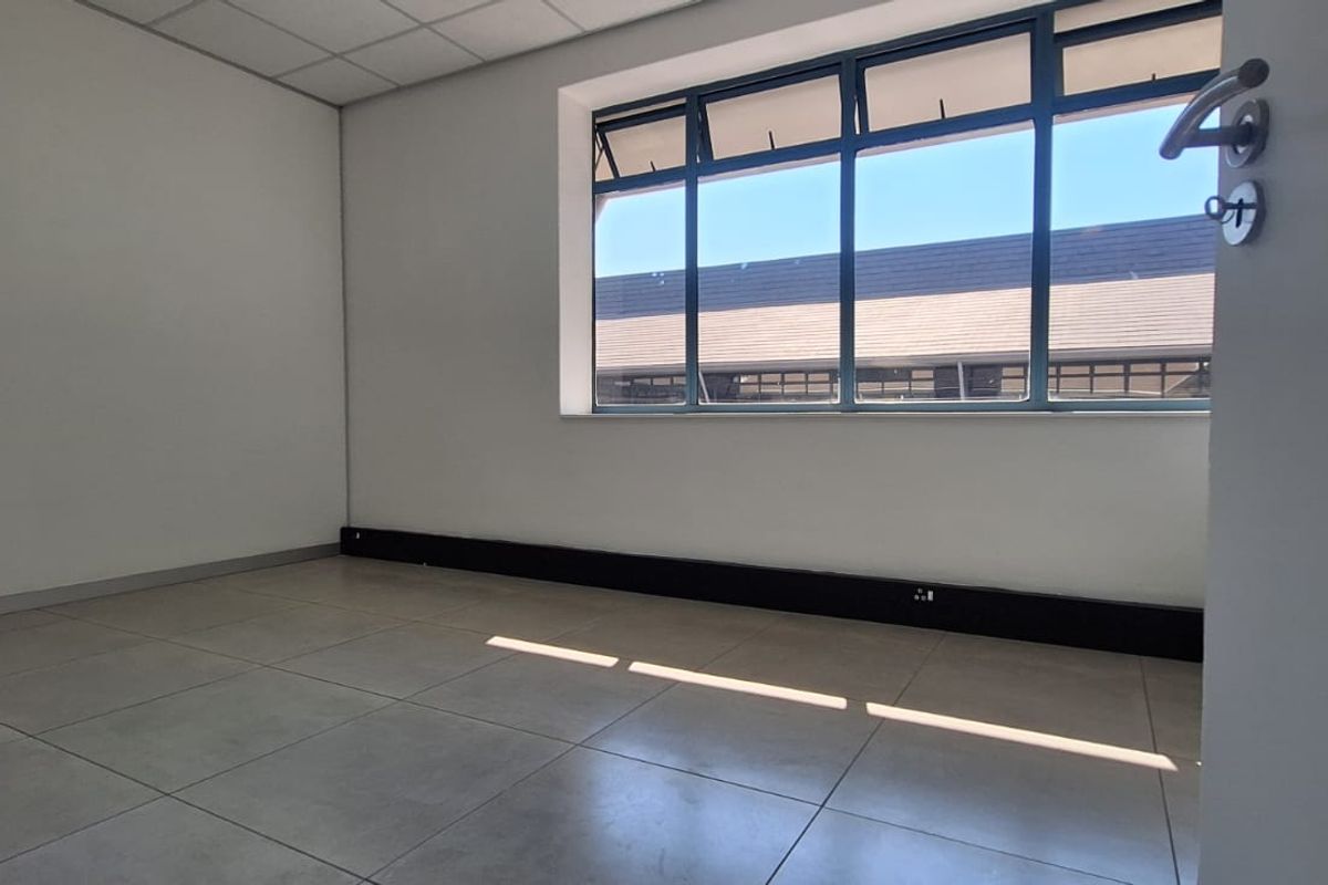 A bright, empty office space featuring large aluminium-framed windows, tiled flooring, and a suspended ceiling, suitable for a professional workspace.