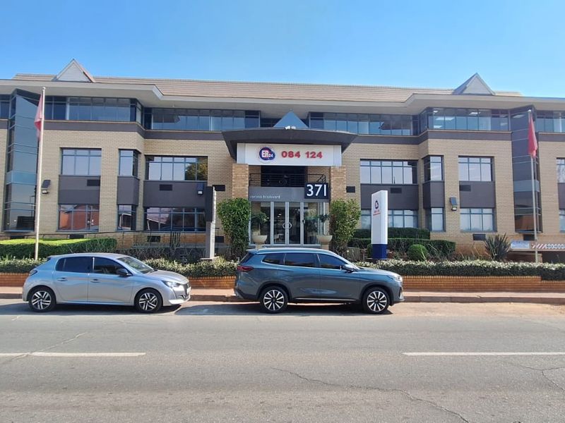 A professional multi-story office building facade featuring brickwork, extensive glazing, and a prominent main entrance, situated along a street front.