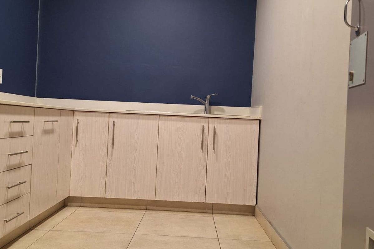 A clean, empty office kitchenette featuring light wood-grain cabinetry, tiled flooring, and a modern sink, providing a functional space for staff.