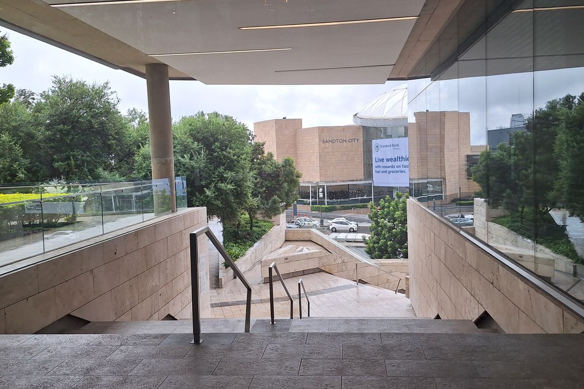 Modern office building entrance featuring a stone staircase, glass balustrades, and architectural stone cladding with views of the surrounding urban landscape.