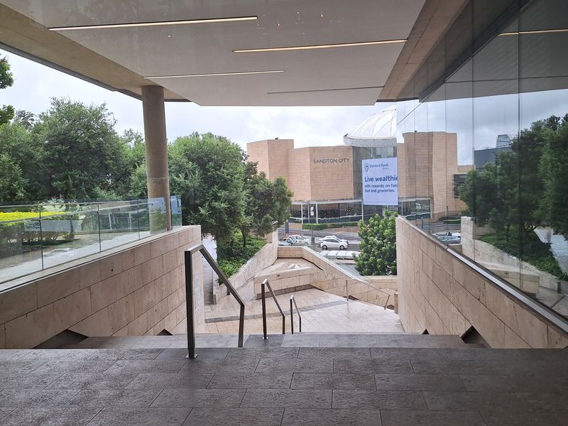 Modern office building entrance featuring a stone staircase, glass balustrades, and architectural stone cladding with views of the surrounding urban landscape.