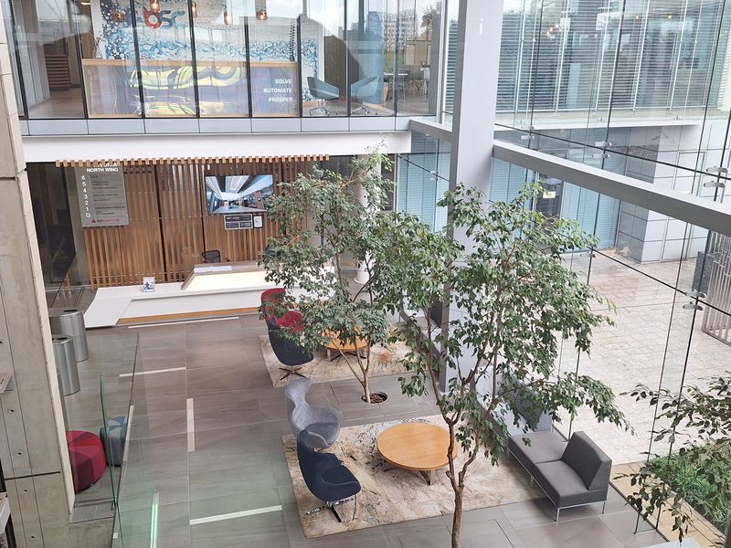 Modern office building atrium featuring a glass curtain wall, reception area, and open-plan seating space with integrated indoor trees.