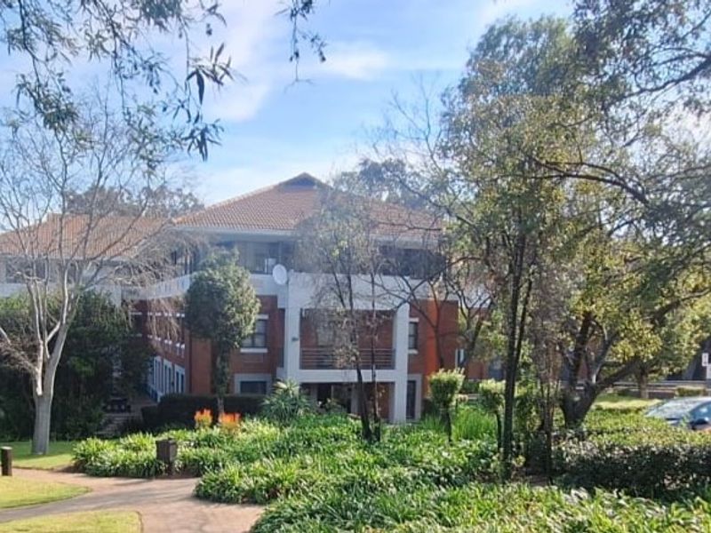 A view of the office building exterior featuring a brick facade, tiled roof, and well-maintained surrounding gardens and walkways.