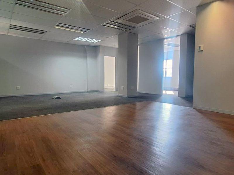 A spacious, vacant open-plan office area featuring a mix of carpet and laminate wood flooring, suspended ceilings, and integrated air conditioning.
