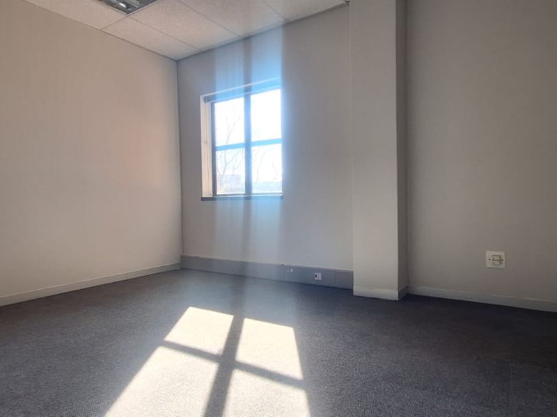 A vacant, well-lit office space featuring neutral walls, carpeted flooring, and a suspended ceiling, suitable for a professional workspace.