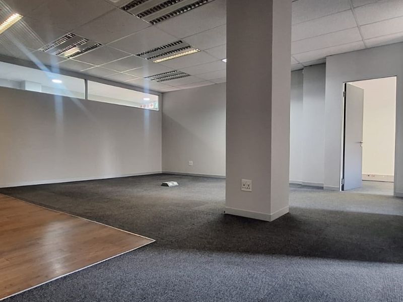 An empty, open-plan office space featuring a mix of carpet and laminate flooring, a structural column, and glass partition walls.