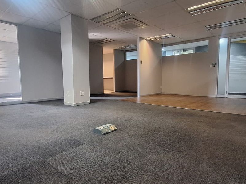 An open-plan office space featuring a mix of carpet and laminate flooring, glass partitions, and recessed ceiling lighting.
