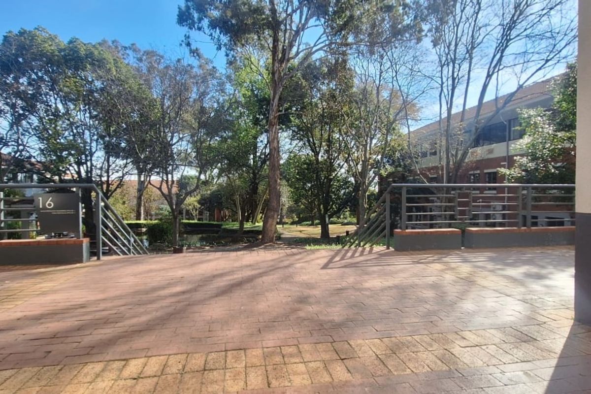 A paved outdoor terrace area featuring metal railings and brick retaining walls, overlooking a landscaped garden setting within the office complex.