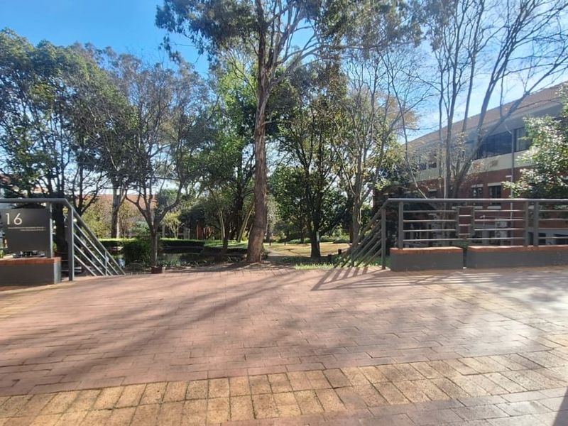 A paved outdoor terrace area featuring metal railings and brick retaining walls, overlooking a landscaped garden setting within the office complex.