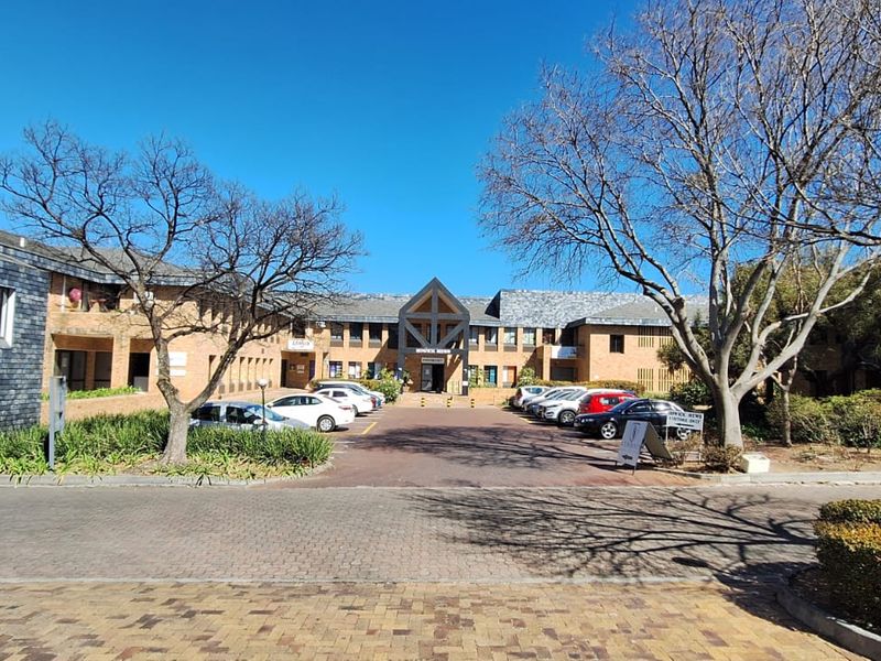Front view of a professional office complex featuring a brick facade, slate roofing, and a paved driveway with ample parking space.