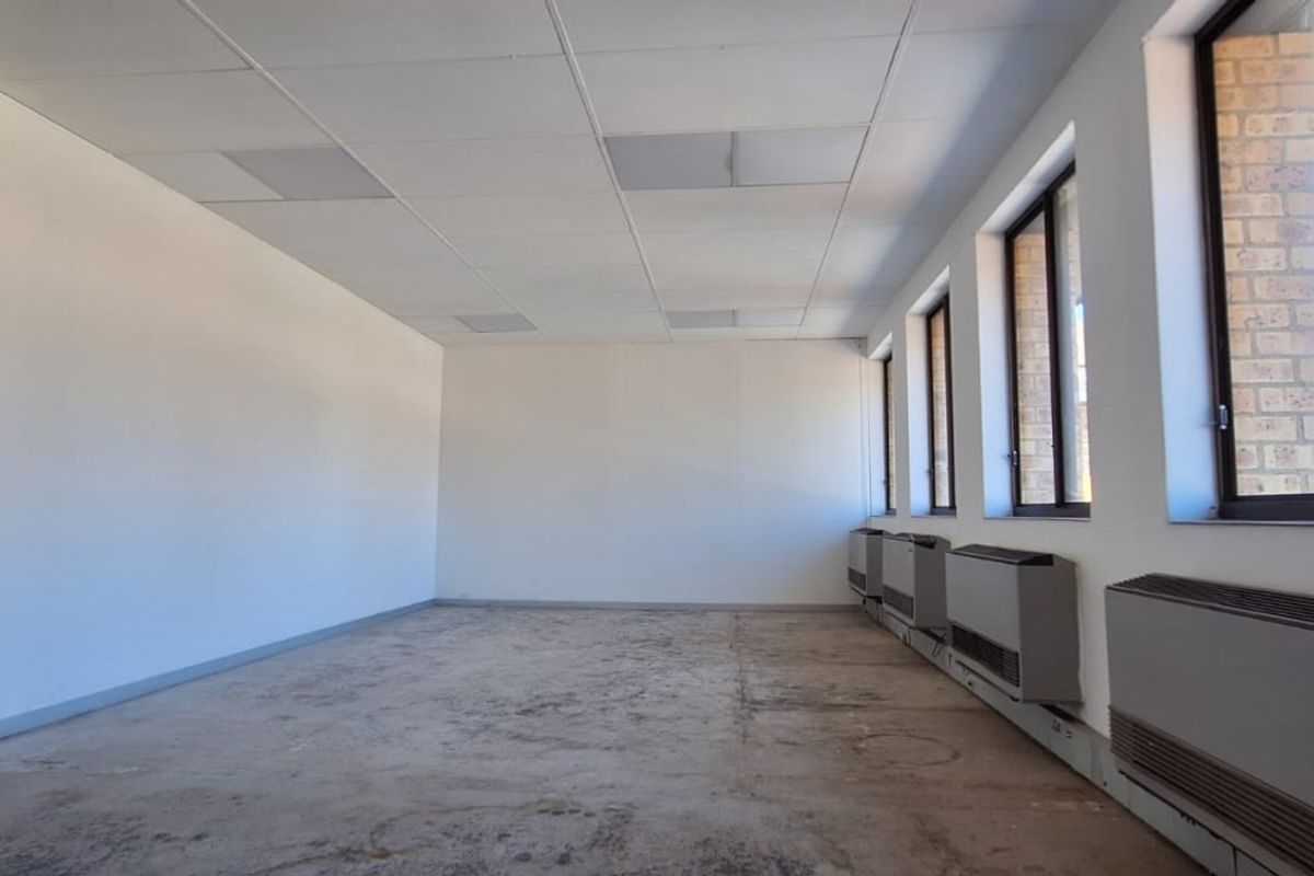 An empty office space featuring a suspended ceiling, large windows for natural light, and wall-mounted air conditioning units, ready for refurbishment.