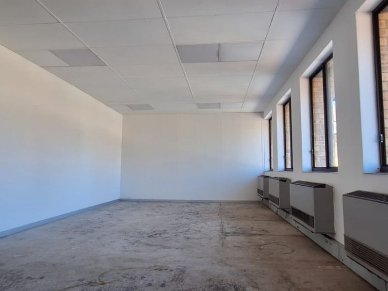 An empty office space featuring a suspended ceiling, large windows for natural light, and wall-mounted air conditioning units, ready for refurbishment.