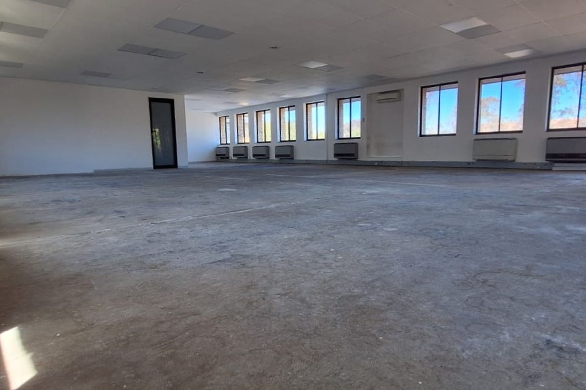 A large, open-plan office space featuring a suspended ceiling, multiple wall-mounted air conditioning units, and expansive windows providing ample natural light.