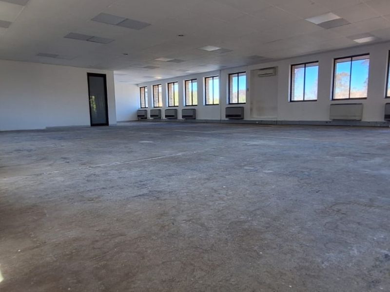 A large, open-plan office space featuring a suspended ceiling, multiple wall-mounted air conditioning units, and expansive windows providing ample natural light.