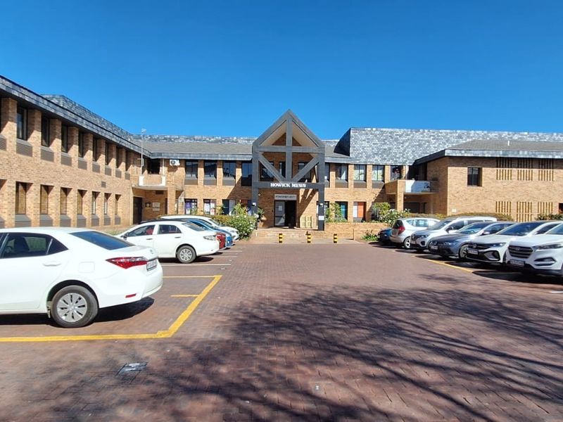 Front elevation of a multi-story brick office complex featuring a paved parking area and a prominent timber-framed entrance structure.