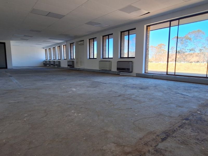 Spacious, open-plan office area featuring large windows, sliding door access, wall-mounted air conditioning units, and exposed concrete flooring ready for refurbishment.