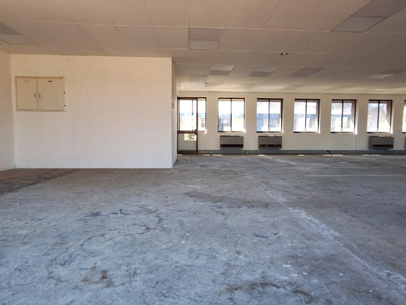 A large, open-plan office space featuring a suspended ceiling, multiple air conditioning units, and expansive windows, currently in need of flooring and wall refurbishment.