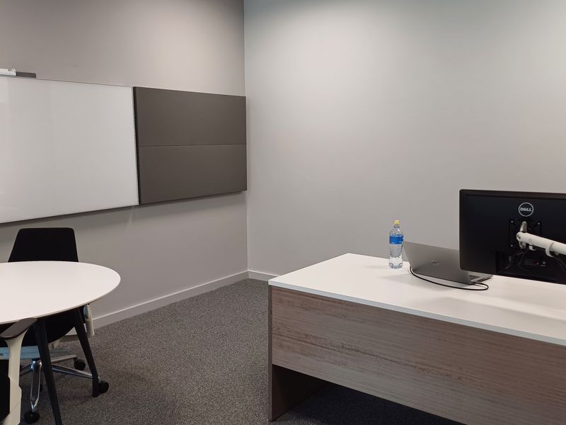 A modern, well-maintained office space featuring a built-in desk, wall-mounted whiteboard, acoustic panels, and neutral carpet flooring, suitable for professional work.