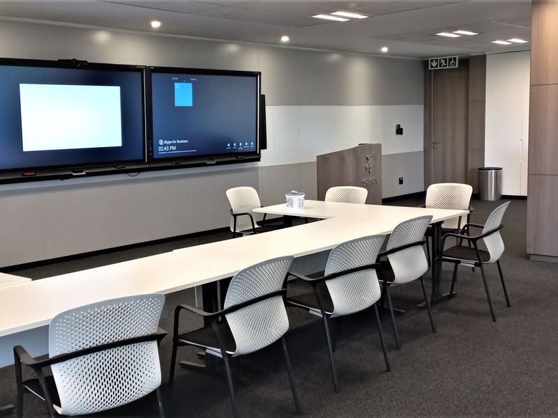 A modern, well-maintained office boardroom featuring integrated wall-mounted display screens, recessed ceiling lighting, and professional carpeted flooring.