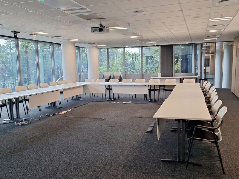A professional office boardroom featuring large floor-to-ceiling windows, a suspended ceiling with integrated lighting, and a U-shaped desk configuration.