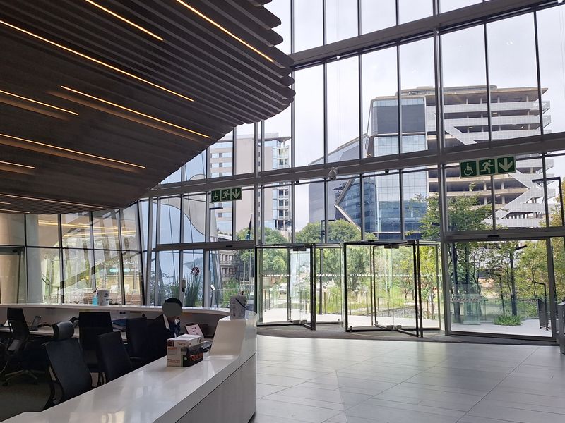 Modern office building entrance lobby featuring a large reception desk, floor-to-ceiling glass facade, and contemporary architectural ceiling design.