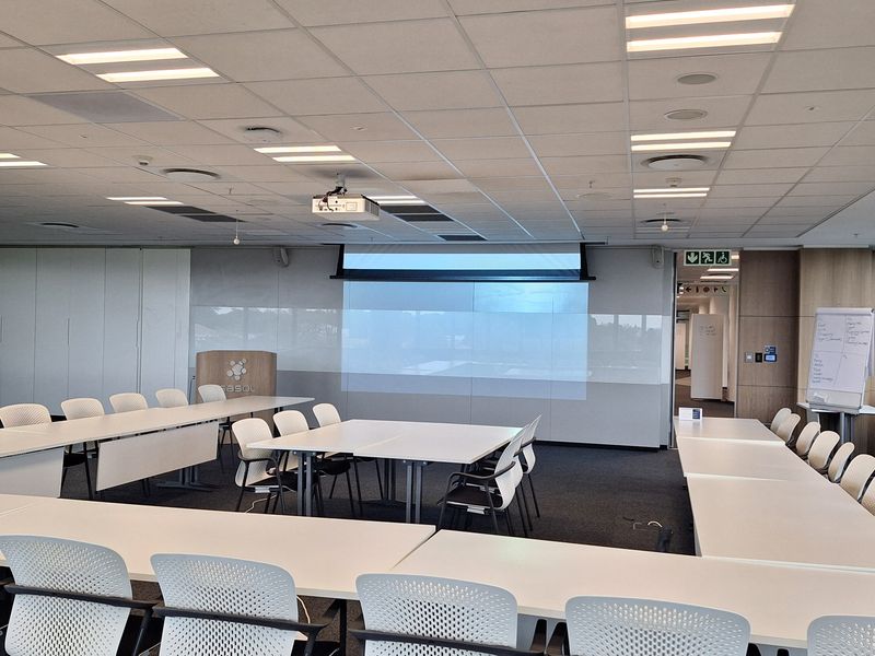 A professional office meeting room featuring a suspended ceiling, integrated projector system, large whiteboard wall, and modular conference table setup.