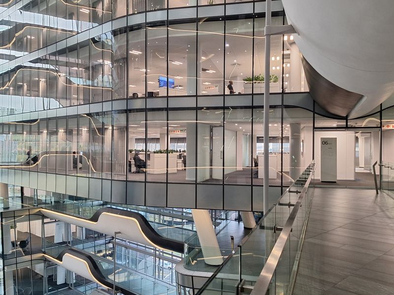 Modern multi-level office atrium featuring extensive glass facades, contemporary architectural design, and open-plan workspace layouts with high-quality finishes.